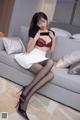 A woman sitting on a couch wearing a black bra and white skirt.