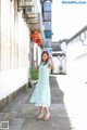 A woman in a blue dress standing on a sidewalk.