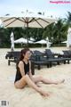 A woman in a black bathing suit sitting on a beach.