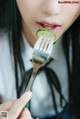 A woman holding a fork with a slice of cucumber on it.