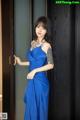 A woman in a blue dress standing in front of a door.