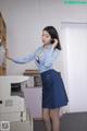 A woman in a blue shirt and skirt standing next to a printer.