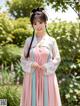 A woman in a pink and blue hanbok standing in a garden.