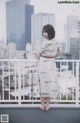 A woman standing on a balcony with a city in the background.