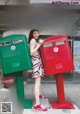 A woman standing next to a red mailbox on a sidewalk.