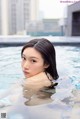 A woman in a swimming pool with a city in the background.