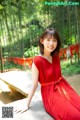 A woman in a red dress sitting on a rock.