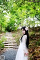 A woman in a white dress standing on a path in the woods.