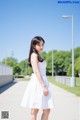 A woman in a white dress standing on a sidewalk.